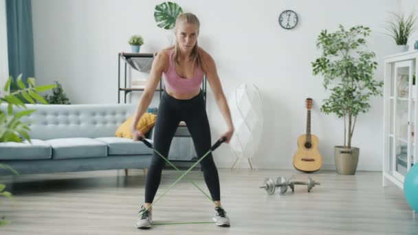 Ritratto di bella bionda in abbigliamento sportivo che fa esercizio a banda di resistenza all'interno della casa moderna — Video Stock