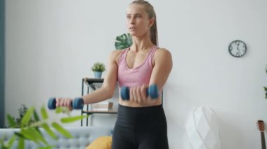 Spor kıyafetleri içinde halterlerle egzersiz yapan güzel genç bir kadının yavaş çekimi.