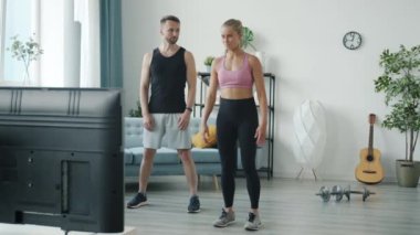 Genç kadın ve erkeğin spor programı izlemesi ve evde zıplama egzersizi yapması.