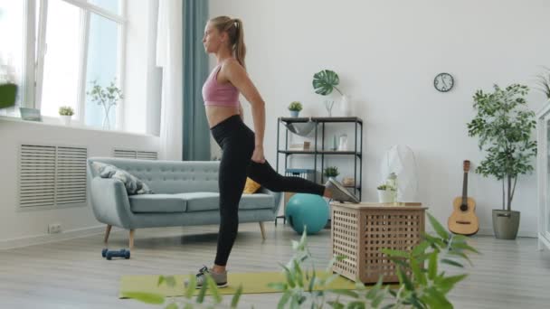Vista lateral da bela jovem fazendo agachamentos em uma perna de treinamento sozinho em casa — Vídeo de Stock