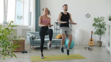 Spor kıyafetli kız ve erkeğin evde spor yaparken ağır çekimde zıplaması.