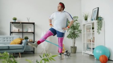Renkli spor kıyafeti giymiş, bantla antrenman yapan, sonra da dans eden çılgın genç adamın ağır çekimleri.