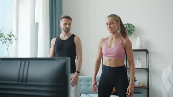 Trage beweging van vrolijke man en vrouw training samen tv kijken en praten in modern appartement — Stockvideo