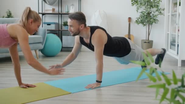 Slow motion van jonge man training thuis met vriendin doen push-ups samen glimlachen — Stockvideo