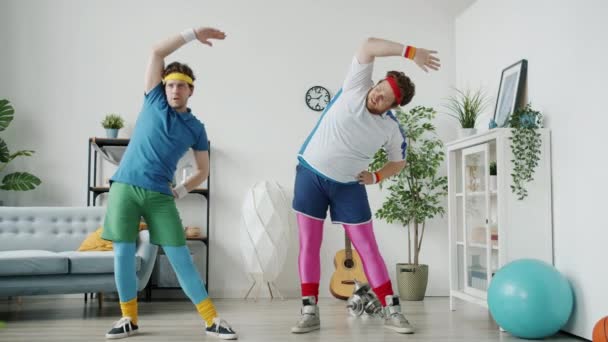 Langsom bevægelse af dovne fyre i sjove farverige tøj træning gør sport i lejlighed – Stock-video