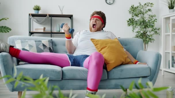 Zeitlupe des faulen übergewichtigen Mannes, der mit Hantel und Gähnen trainiert und dann zu Hause auf dem Sofa schläft — Stockvideo