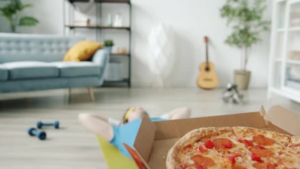 Långsamma rörelser av bisarra idrottare som gör crunches och sträcker ut armarna till pizza träning ensam i lägenheten — Stockvideo