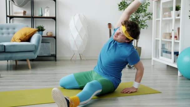 Vážný chlap v pestré sportovní oblečení dělá jóga cvičení na světlé podložce v bytě — Stock video