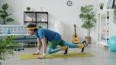 Renkli kıyafetli komik bir sporcunun ağır çekimde minder üstünde antrenman yapması ve sonra yorgun hissetmesi.