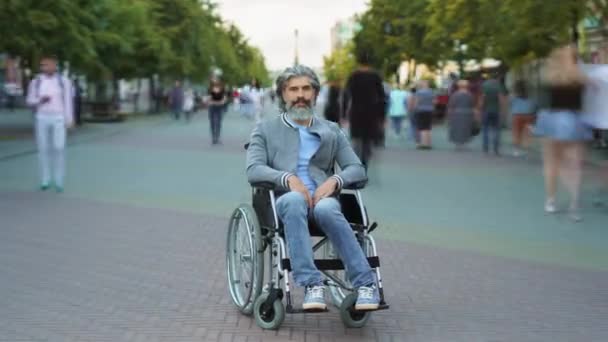 Gros plan portrait d'un homme mature handicapé assis en fauteuil roulant dans une rue urbaine animée avec des gens se précipitant autour — Video