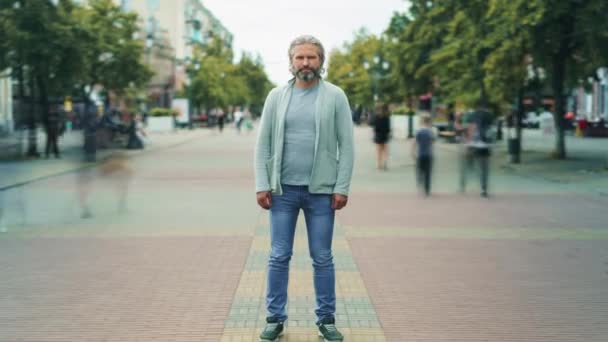 Zoom en lapso de tiempo retrato de hombre maduro serio de pie fuera en la calle con la gente corriendo alrededor — Vídeos de Stock