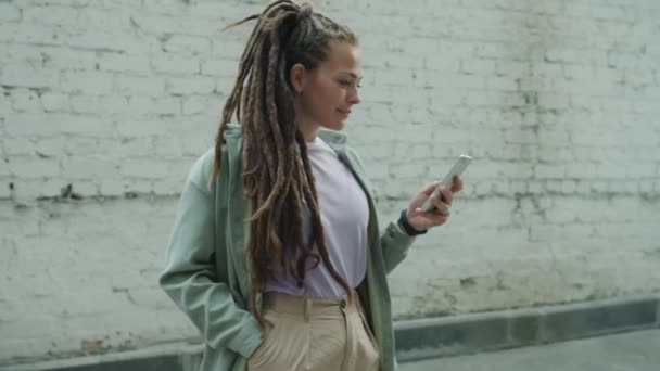 Portré gyönyörű fiatal nő raszta segítségével smartphone sms kint áll — Stock videók