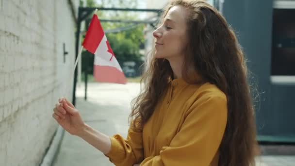 Portret van een gelukkige jongedame die met een Canadese vlag zwaait en buiten in de stad staat te glimlachen — Stockvideo