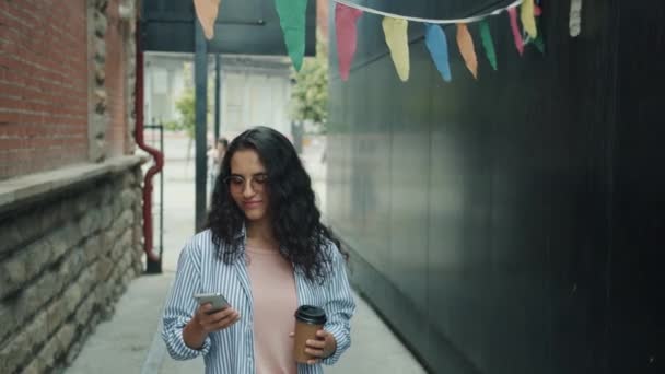 Slow motion av söt asiatisk dam med hjälp av smartphone och hålla för att gå kaffe i urban street — Stockvideo