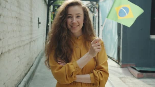 Slow motion porträtt av glad flicka med brasiliansk flagga står utomhus i modern stad — Stockvideo