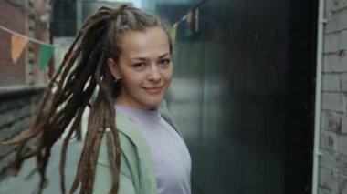 Rastalı güzel bir genç bayanın portresi kameraya dönüyor ve şehirde gülümsüyor.