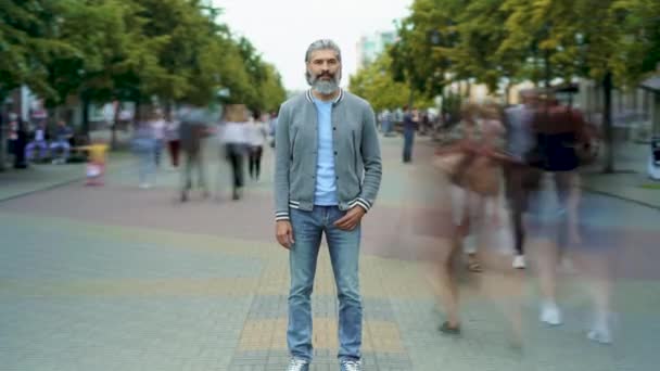 Zoom-in time lapse portrait of confident mature guy standing outdoors in street among crowd of people — Stock Video