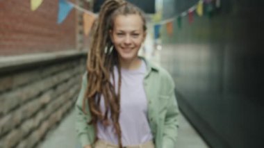 Rastalı güzel bir kızın zoom portresi. Şehirde durmuş kameraya bakarak gülümsüyor.