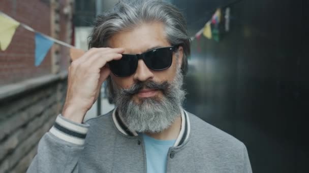 Portrait d'un homme mature confiant enlevant des lunettes de soleil noires et regardant la caméra avec un visage sérieux debout à l'extérieur — Video
