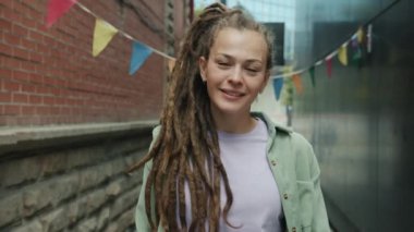 Rasta sallayan, gülümseyen ve dışarıda selamlaşan çekici bir kadının portresi.