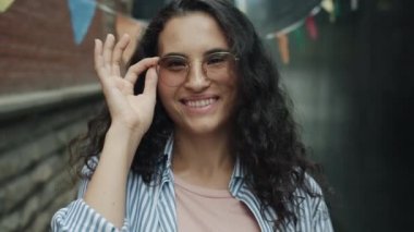 Çekici Asyalı bir kızın portresi. Gözlüklere dokunuyor. Kırpıyor ve gülüyor.