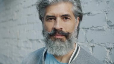 Açık havada tek başına duran gri saçlı ve sakallı olgun bir adamın yakın plan portresi.