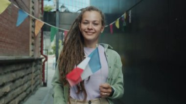 Rastalı güzel bir kadının yavaş çekim portresi Fransız bayrağı sallıyor ve kentsel arka planda gülümsüyor.