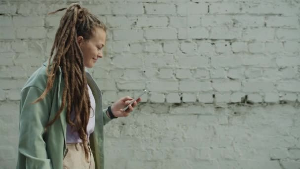 Portrait of beautiful girl with dreadlocks using smart phone enjoying social media and smiling walking outside — Stock Video