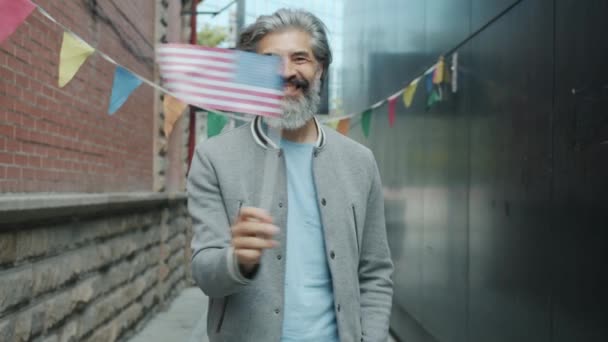 Langzame beweging van vrolijke grijsharige man zwaaiend met Amerikaanse vlag en glimlachend buiten — Stockvideo