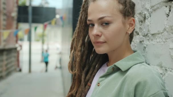 Portrait of creative girl with dreads looking at camera with no emotion standing outside alone — Stok Video
