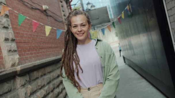 Rotativa retrato de menina atraente com dreadlocks em pé fora na cidade sorrindo olhando para a câmera — Vídeo de Stock