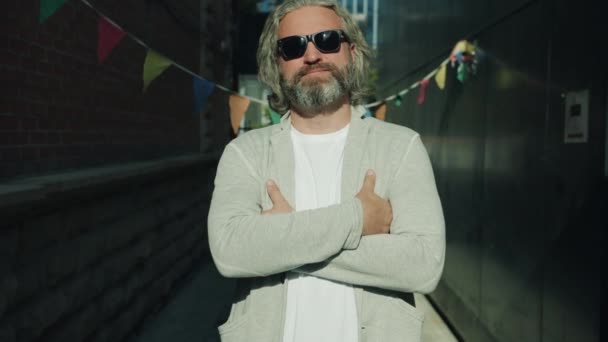 Slow motion portret van een stijlvolle volwassen man die buiten staat met een trendy zonnebril en naar de camera kijkt — Stockvideo