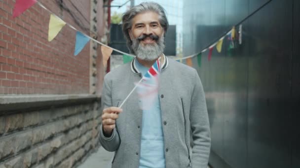 Медленное движение веселого взрослого англичанина, размахивающего британским национальным флагом и улыбающегося стоя на улице — стоковое видео