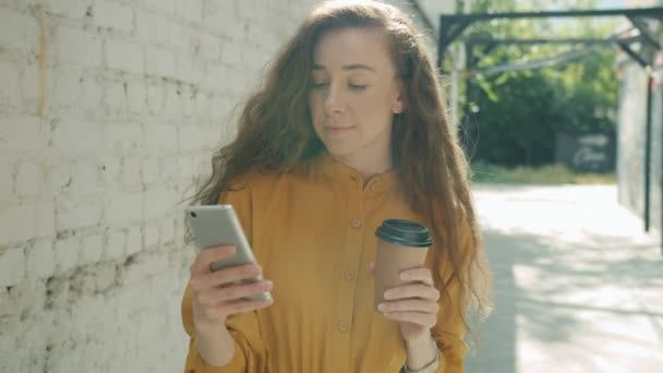 Movimento lento de uma jovem pensativa usando a bebida do smartphone tomar café em pé fora na cidade — Vídeo de Stock
