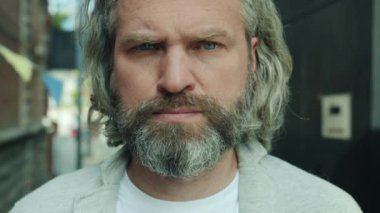 Yetişkin sakallı bir adamın ciddi bir yüzle kameraya bakışının yavaş çekim portresi.
