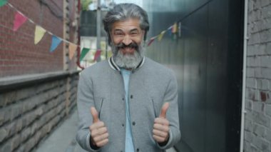 Heyecanlı adamın yavaş hareket eden portresi. Başparmak hareketi yapıyor ve şehir dışında gülüyor.