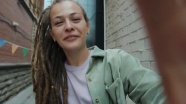 Rasta saçlı çekici bir kız konuşuyor ve el sallıyor. Kameraya bakıyor. Dışarıdan video çağrısı yapıyor.