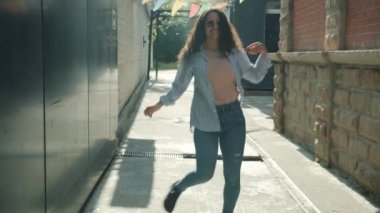 Güneşli bir yaz gününde şehir caddesinde dans eden çekici, modern bir kadının yavaş çekim portresi.