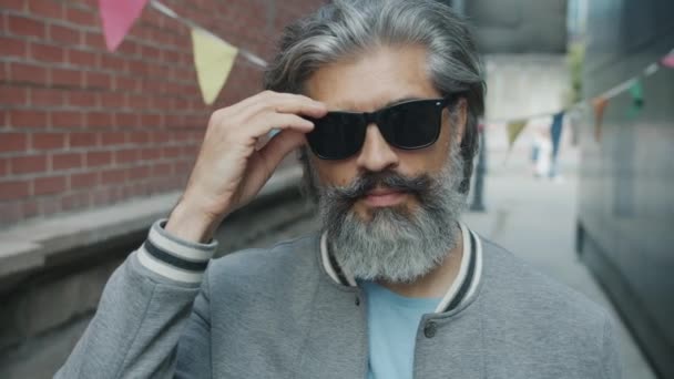 Retrato de una persona madura seria levantando gafas de sol negras y cabeceando con la cabeza con la aprobación de pie al aire libre — Vídeos de Stock