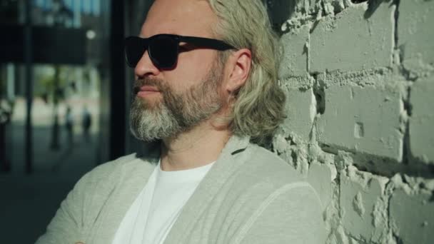 Retrato de primer plano de un hombre barbudo guapo con gafas de sol girando hacia la cámara exterior — Vídeos de Stock