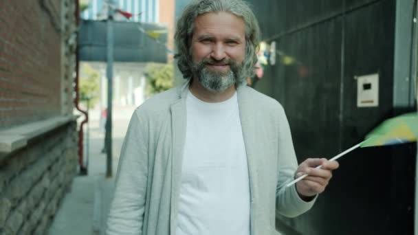 Porträt eines gut aussehenden Mannes mittleren Alters, der die brasilianische Flagge schwenkt und vor dem Hintergrund der Stadt lächelt — Stockvideo