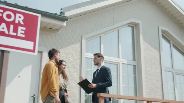 Menina e cara discutindo acordo de habitação com agente imobiliário ao ar livre perto de bela casa suburbana — Vídeo de Stock