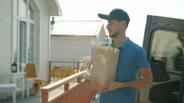 Erkek kurye, banliyö bölgesindeki erkek müşteriye kağıt torbayla organik gıda taşıyor. — Stok video