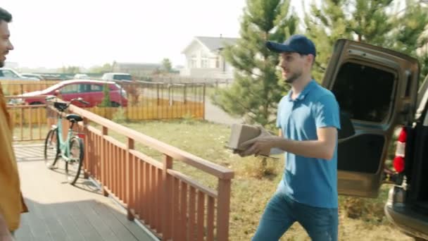 Young man customer receiving parcel from delivery guy signing paper outdoors at front door — Stock Video
