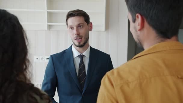 Портрет агента з нерухомості, який розмовляє з клієнтами в приміщенні в новому будинку посміхається — стокове відео