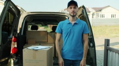 Ticari kamyonetin yanında duran teslimatçının portresi. Kollarını kavuşturup kameraya bakarken gülümsüyor.