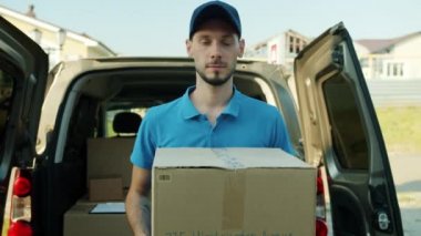 Karton kutu taşıyan üniformalı bir teslimatçının portresi. Elinde paketlerle minibüsün yanında duruyordu.