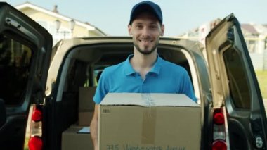 Dost canlısı kuryenin teslimat aracının yanında elinde mallarla birlikte ağır çekimde portresi.