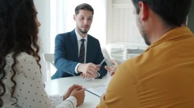 Genç bir çift ev satın alıyor. Kapalı mekanda mutlu simsarlarla konuşuyorlar.