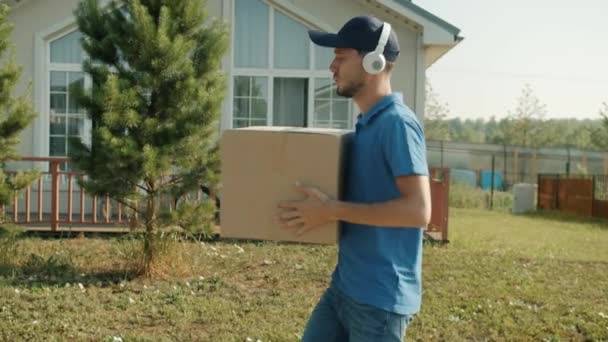 Trabajador de entrega feliz llevando caja de cartón y disfrutando de la música en auriculares bailando divirtiéndose — Vídeos de Stock